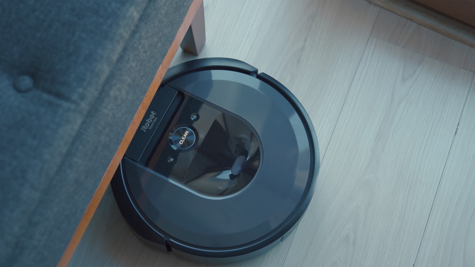 A robot vacuum on a wooden floor, reversing out from under a sofa