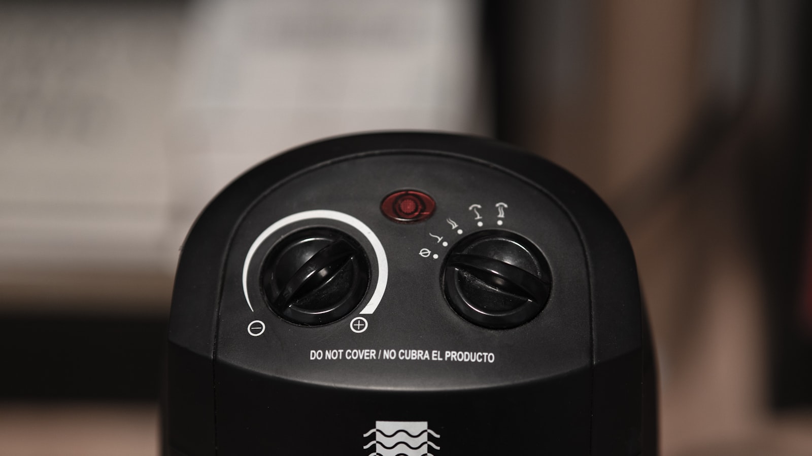 Close-up of the black control panel on a portable fan heater, with two dials, a red indicator light and a printed DO NOT COVER warning