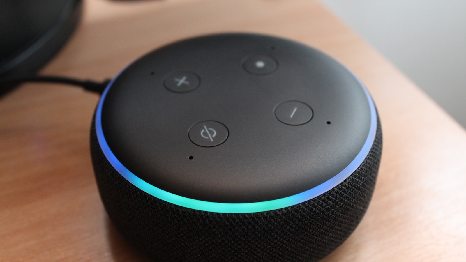 An Amazon Echo Dot on a wooden table with its light ring lit blue