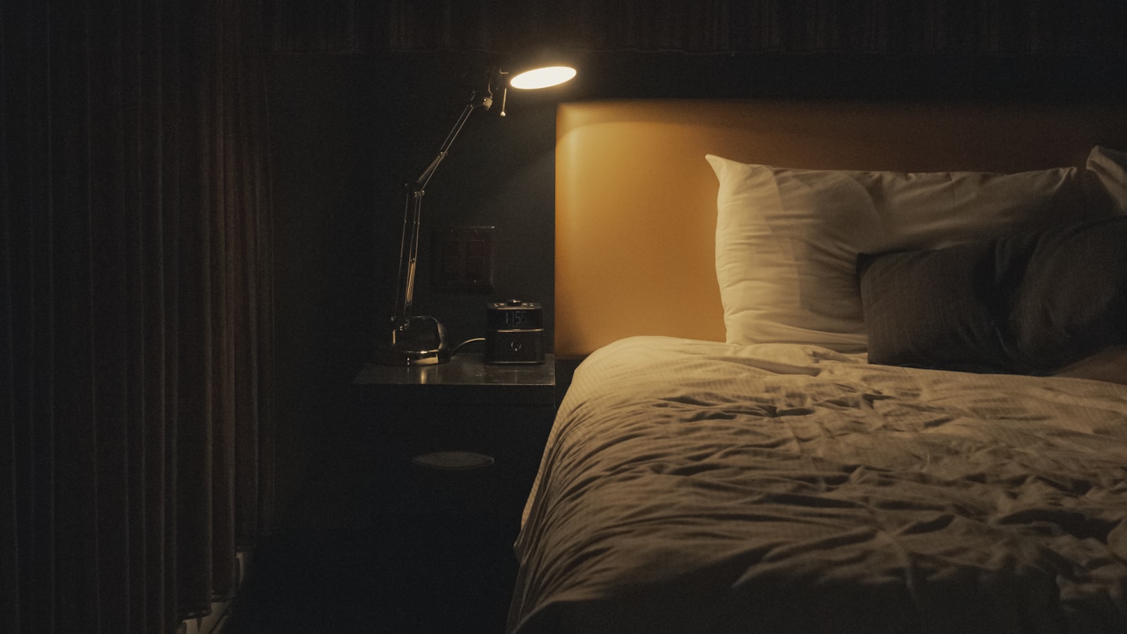 A dimly lit bedroom at night, with a lamp and a clock on the bedside table