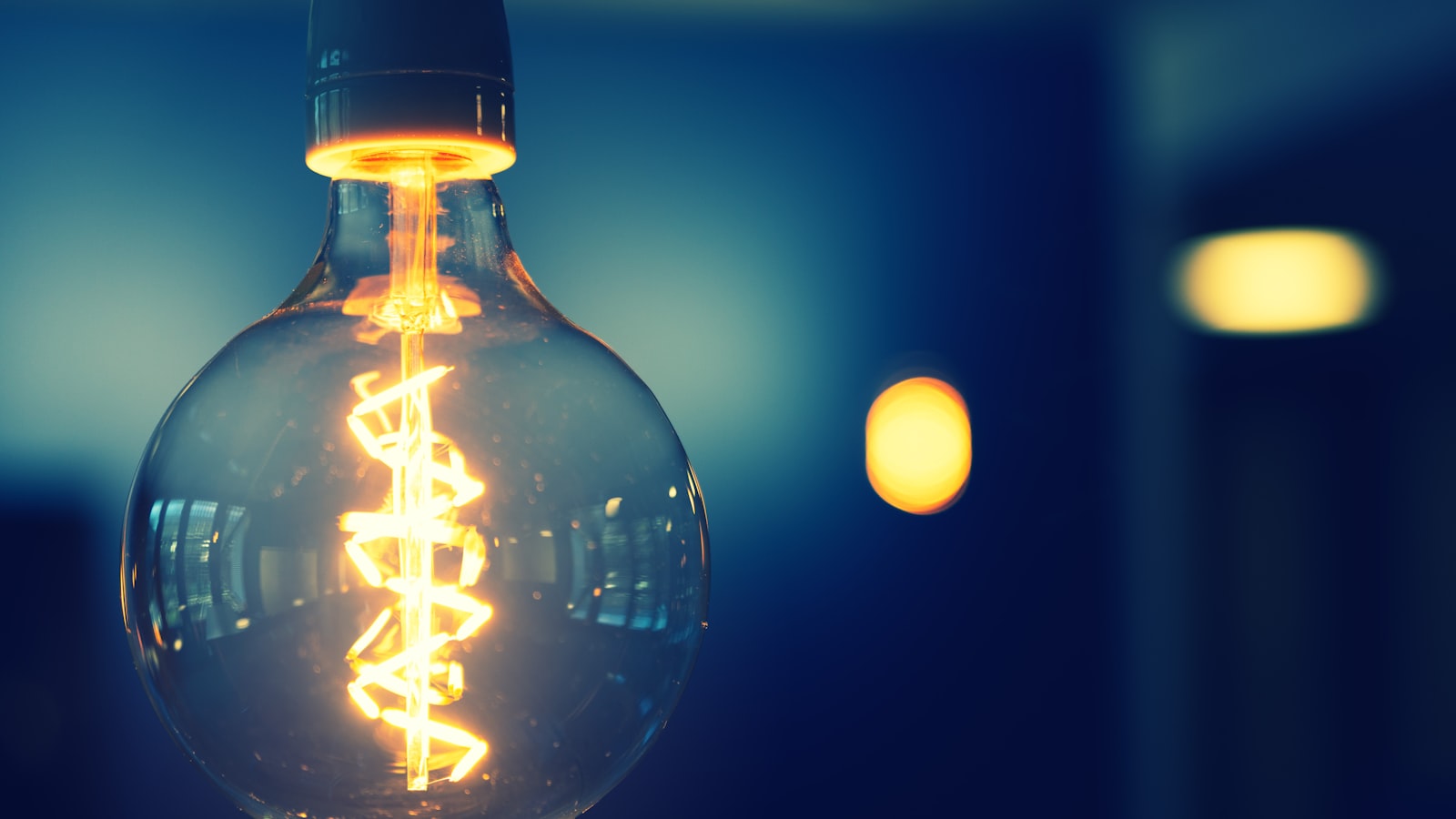 A filament light bulb lit in its socket, the screw cap visible at the top
