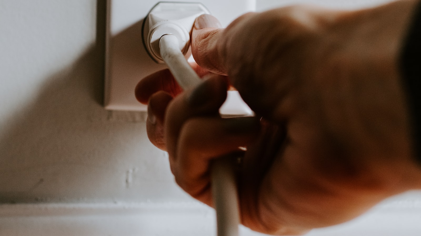 A hand plugging a lead into a wall socket